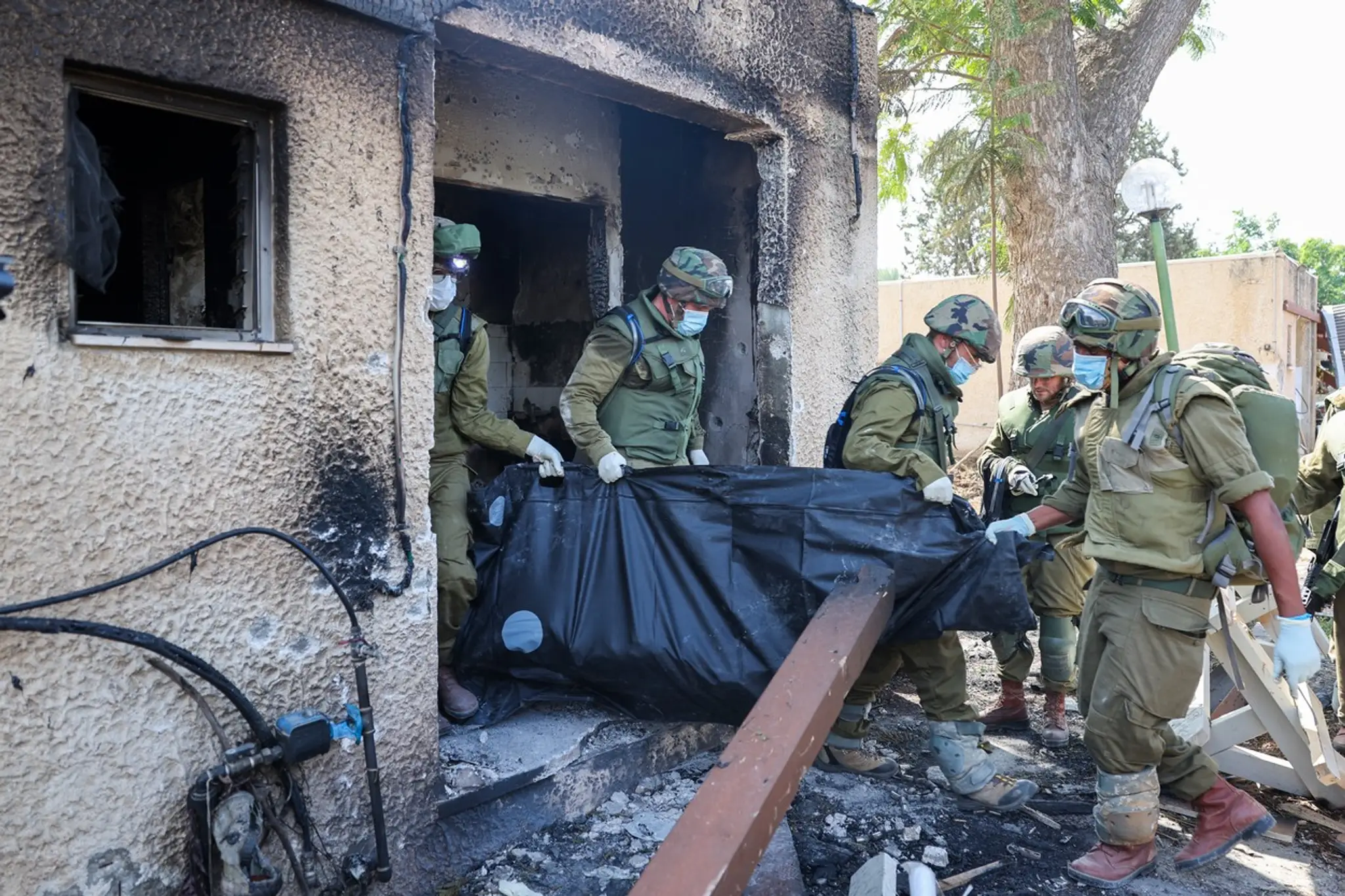 Izraelskí vojaci vynášajú telá z domov v kibuci Kfar Aza