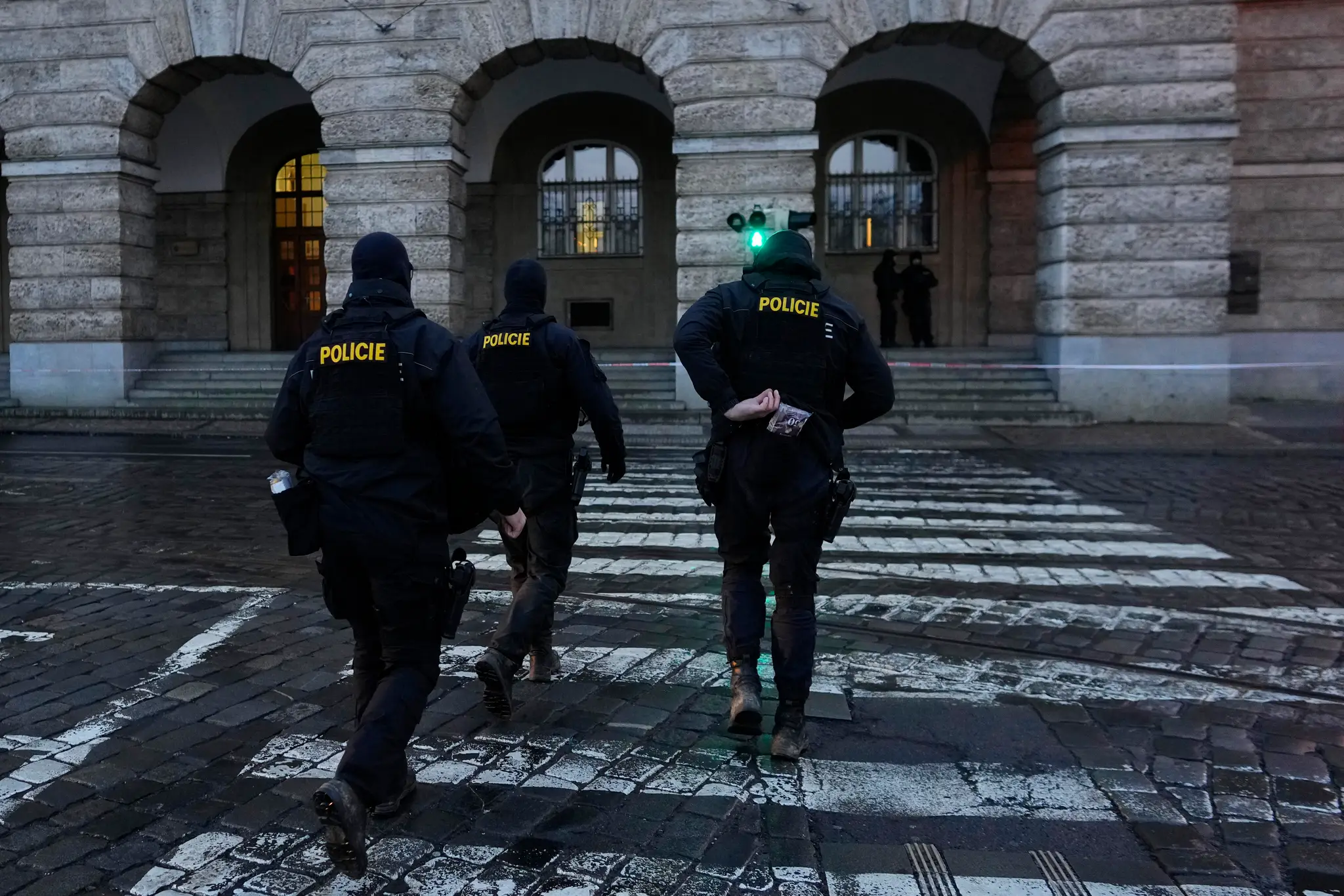 Policajti kráčajú pred budovou Filozofickej fakulty Univerzity Karlovej (FF UK) po streľbe v centre Prahy 22. decembra 2023. 