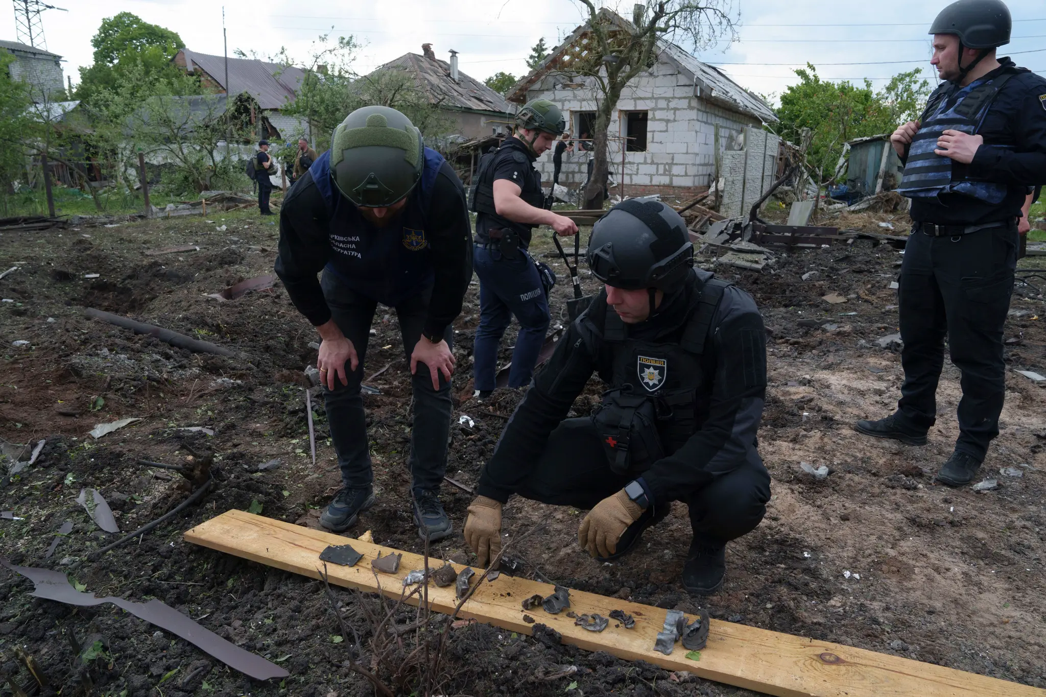 Ukrajinský policajt a prokurátor pre vojnové zločiny si prezerajú úlomky bomby pred poškodeným domom po ruskom ostreľovaní obytných častí mesta Charkov.