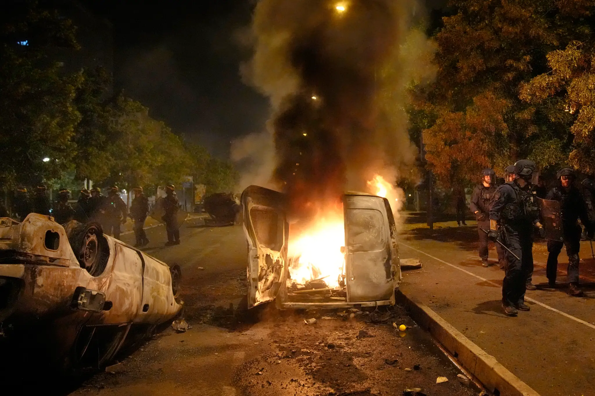 Policajti kráčajú okolo horiacich áut v meste Nanterre na predmestí Paríža.