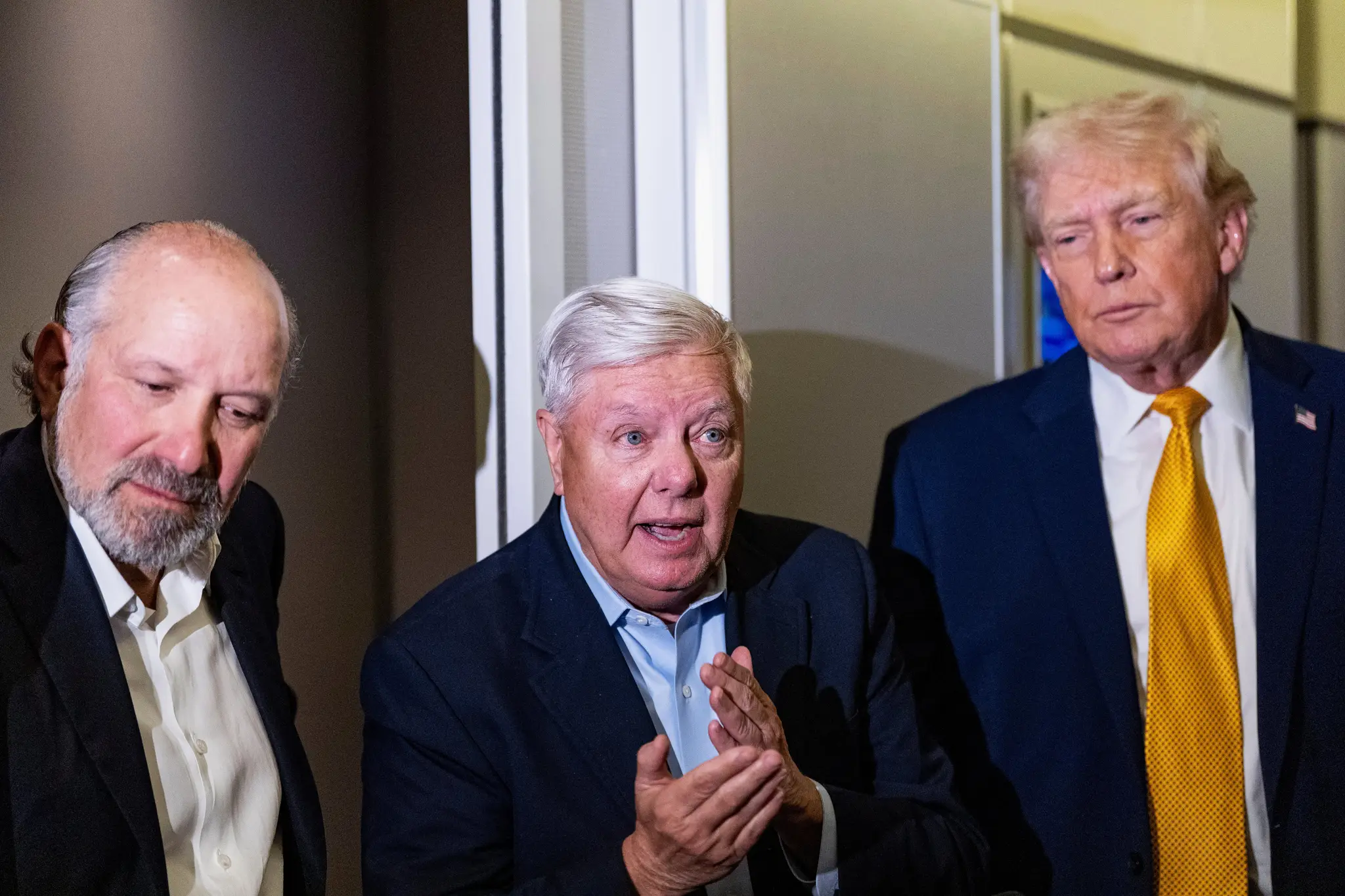 Prezident Donald Trump v sprievode ministra obchodu Howarda Lutnicka (vľavo) a senátora Lindseyho Grahama (R-S.C.) hovorí s novinármi počas letu v lietadle Air Force One.