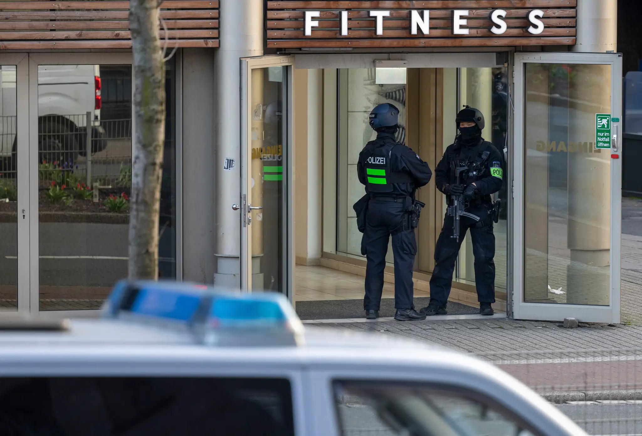 Ozbrojení policajti stoja pred vstupom do fitnescentra.