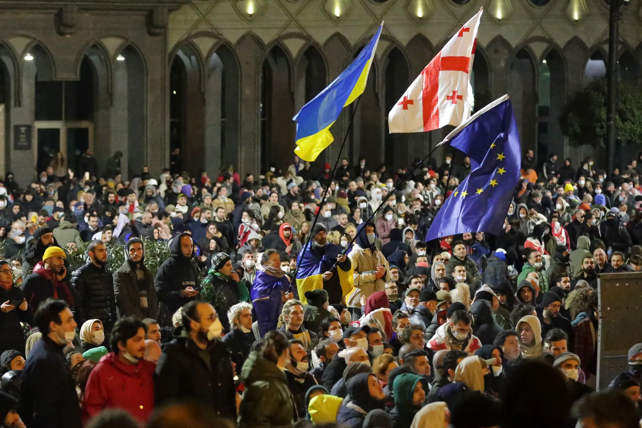 Demonštranti mávajú vlajkami zľava Ukrajiny, Gruzínska a Európskej únie počas protestu pred budovou parlamentu v Tbilisi.