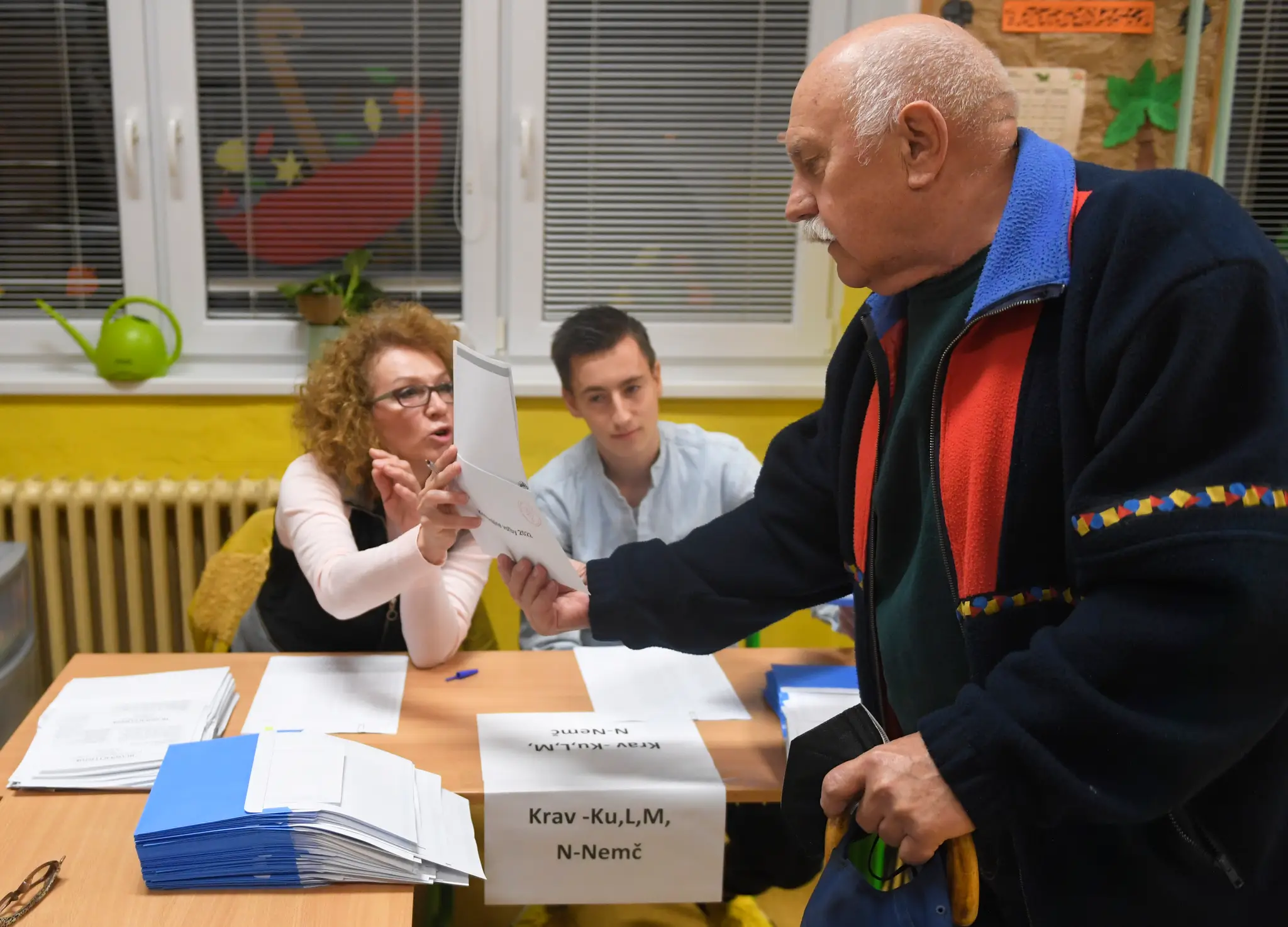 Na snímke volič si preberá hlasovacie lístky od členky volebnej komisie vo volebnej miestnosti na ZŠ Hroncova v Košiciach.