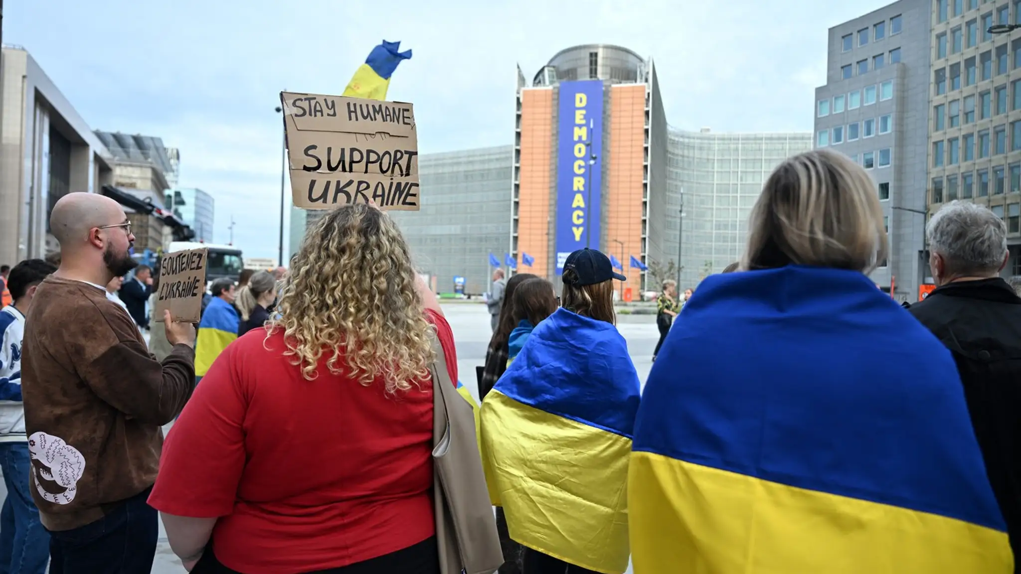 Ukrajinci sa zhromažďujú s ukrajinskými vlajkami a kuframi pred budovou Rady Európskej únie.