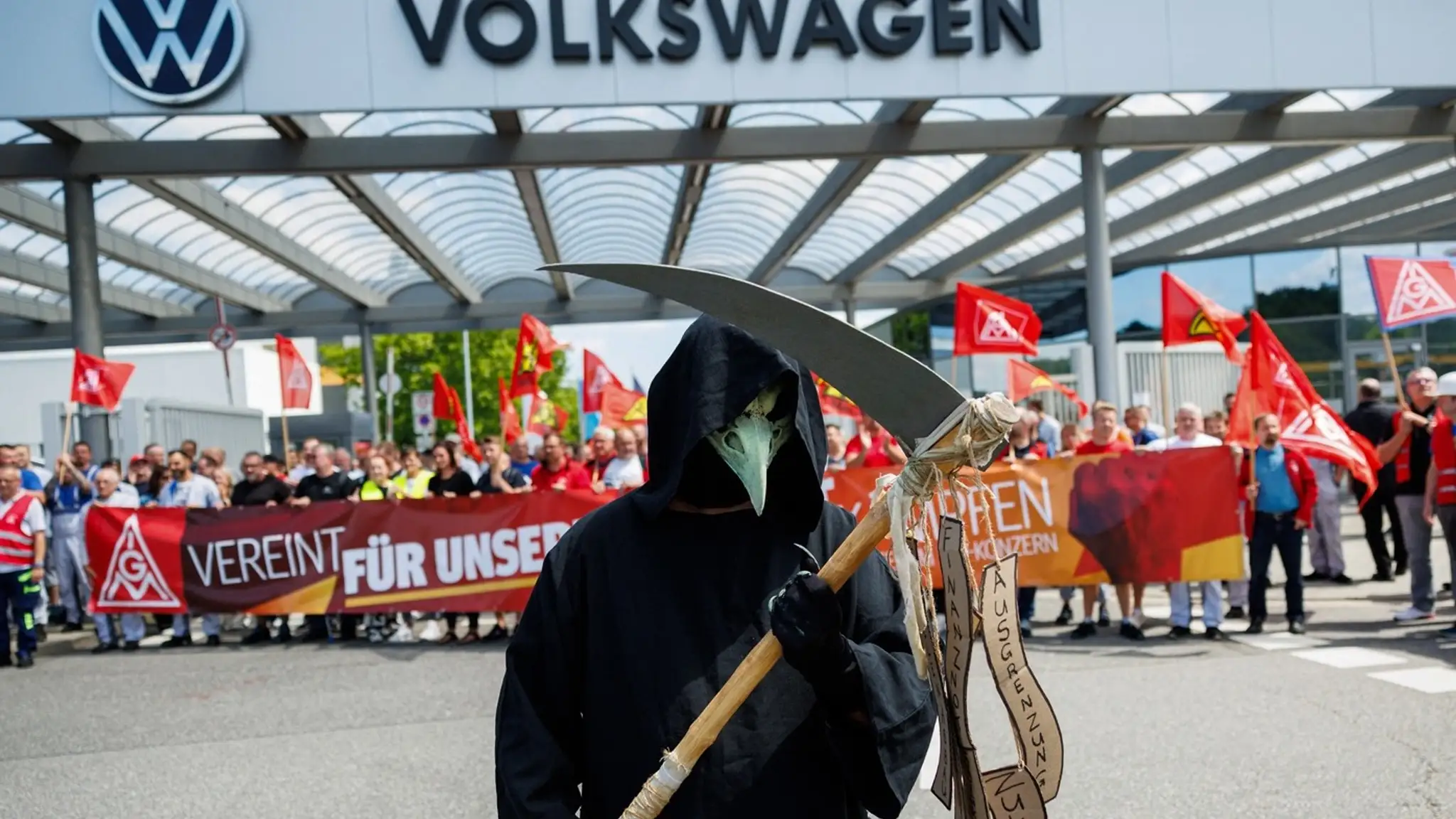 Účastník v kostýme Smrťky stojí pred vchodom do závodu, zatiaľ čo zamestnanci nemeckého výrobcu automobilov Volkswagen.