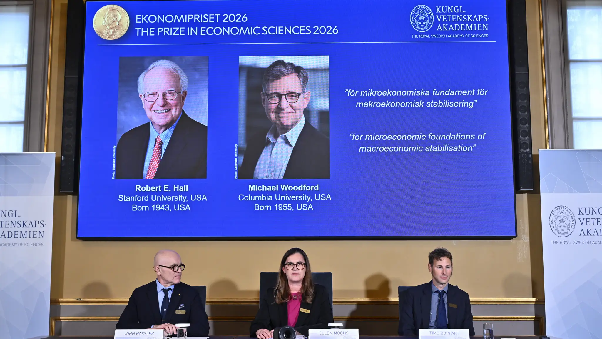 Na veľkoplošnej obrazovke sú americkí ekonómovia Robert E. Hall (vľavo) a Michael Woodford, ktorým udelili Nobelovu cenu za ekonómiu za rok 2026.