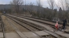 VIDEO: K nešťastiu chýbalo málo. Muž s dieťaťom prechádzali na bicykli cez koľajnice, o pár sekúnd tade prefrčal vlak