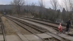 VIDEO: K nešťastiu chýbalo málo. Muž s dieťaťom prechádzali na bicykli cez koľajnice, o pár sekúnd tade prefrčal vlak