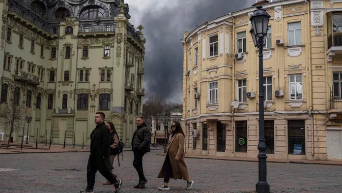 Na archívnej snímke z 3. apríla 2022 ľudia kráčajú po ulici, v pozadí dym stúpa k oblohe po ostreľovaní v ukrajinskom meste Odesa.