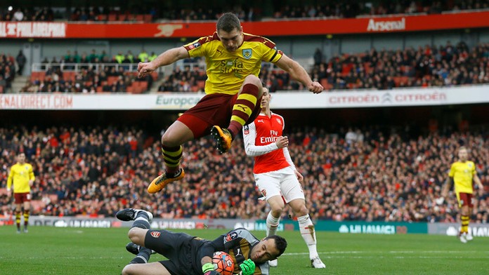 Hráč Sam Vokes (Burnley) skáče ponad brankára Davida Ospinu (Arsenal).