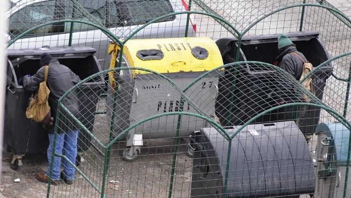 Bezdomovci vyberajú odpad z kontajnerov.