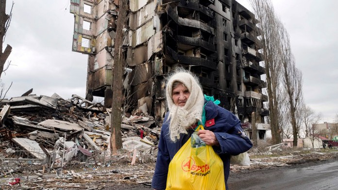 Staršia žena prechádza okolo obytného domu zničeného pri ruskom ostreľovaní.