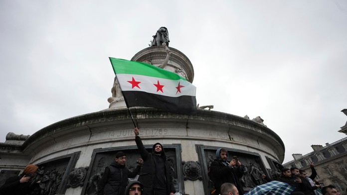 Sýrčania žijúci vo Francúzsku mávajú národnou zástavou počas zhromaždenia na Námestí republiky po páde sýrskeho vládneho režimu v Paríži.