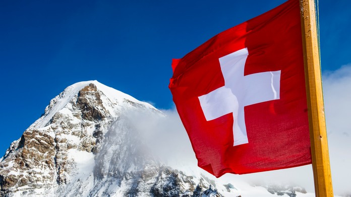 Štátna vlajka Švajčiarska veje a v pozadí Alpy.