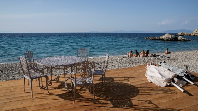 Ľudia sedia na pláži pred tavernou v meste Kokkari na gréckom ostrove Samos.