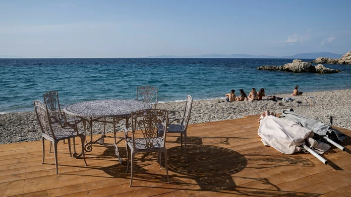 Ľudia sedia na pláži pred tavernou v meste Kokkari na gréckom ostrove Samos.