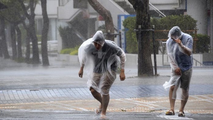 Ľudia kráčajú s ťažkosťami na ulici počas silného vetra a dažďa s príchodom super tajfúnu Vongfong