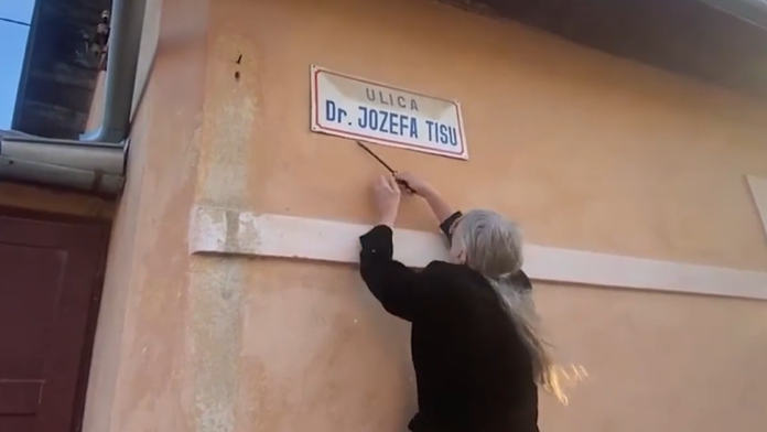 Na snímke občiansky aktivista strháva tabuľu ulice Jozefa Tisa vo Varíne.