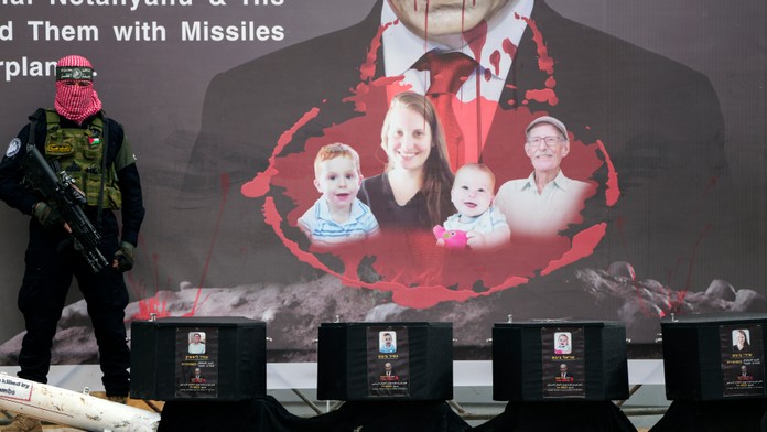 Na snímke palestínsky bojovník stojí pri rakvách s telesnými pozostatkami štyroch izraelských rukojemníkov počas odovzdania ich tiel.