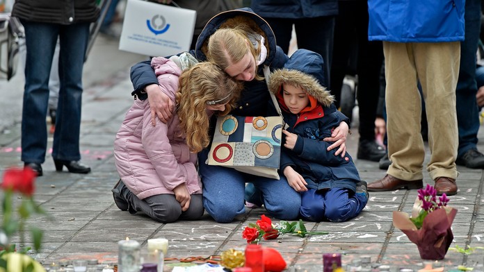 Žena s deťmí kľačí na pamiatku obetí  bombových útokov v Bruseli.