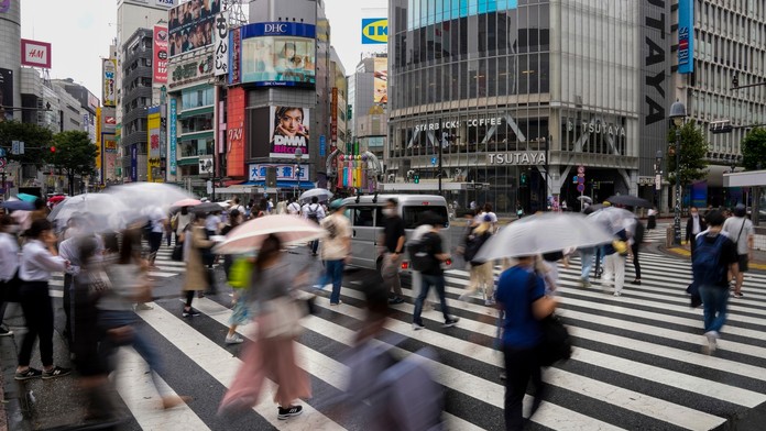 Ľudia kráčajú s dáždnikmi cez križovatku v Tokiu.