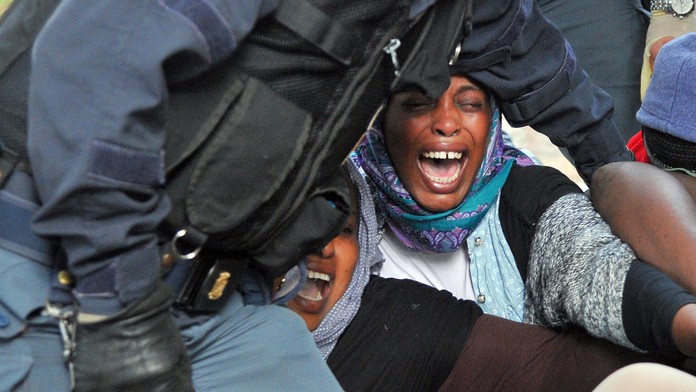 Policajti odnášajú ženy migrantov z hraničného priechodu