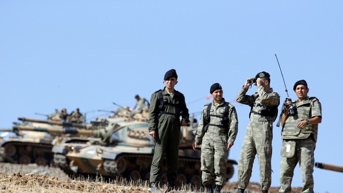 Tureckí vojaci sledujú okolie pri tureckom tanku rozmiestnenom pri hranici so Sýriou