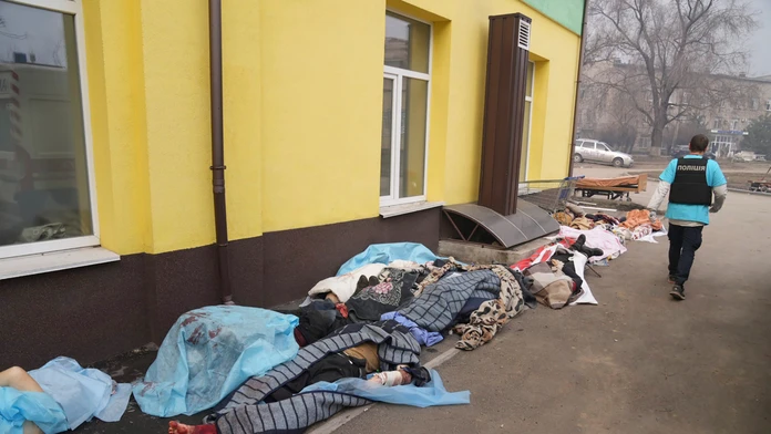 Policajt kráča popri mŕtvych telách pred nemocnicou v Mariupole.