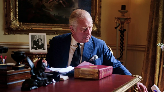 Nový britský kráľ Karol III. sedí za pracovným stolom a vyberá z oficiálnej červenej krabice korešpondenciu.
