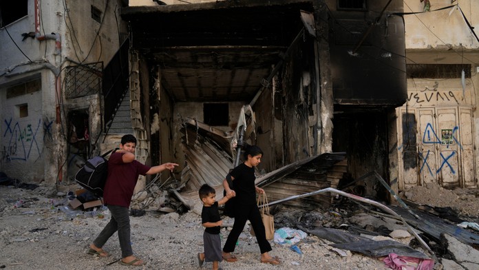 Palestínski utečenci kráčajú okolo zhoreného domu.