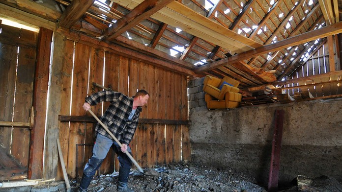 Muž odstraňuje nánosy bahna zo stodoly deň po prietrži mračien vo Vlkovciach.