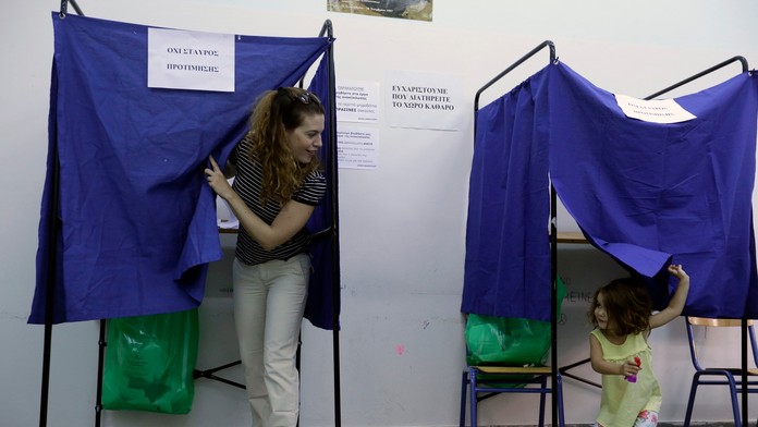 Žena s dieťaťom vychádzajú spoza plenty vo volebnej miestnosti v Aténach.