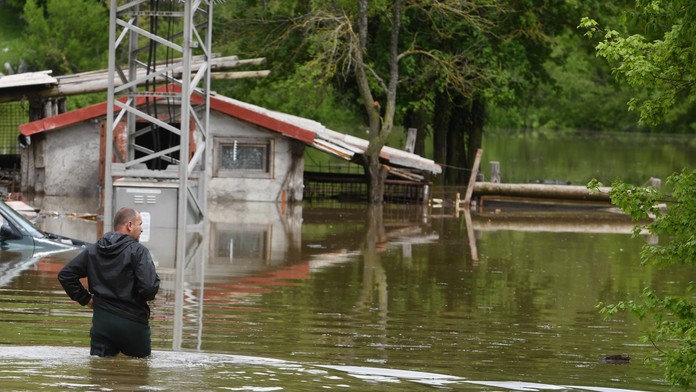 Muž stojí po kolená vo vode po povodniach v Chorvátsku.