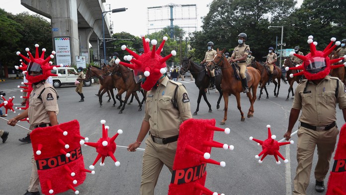Indickí policajti kráčajú v prilbách v tvare nového typu koronavírusu počas akcie zameranej na prevenciu šírenia koronavírusu.