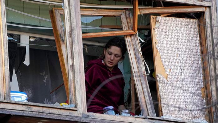 Žena stojí pri rozbitom okne vo svojom byte po ruskom bombovom útoku v Kyjeve.