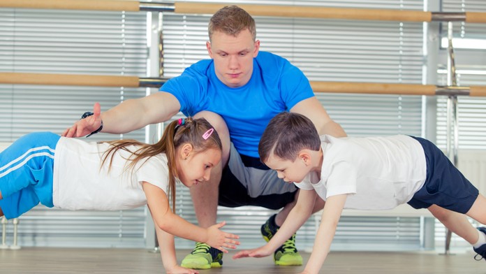 Na snímke sú dve deti, ktoré cvičia a učiteľ. 