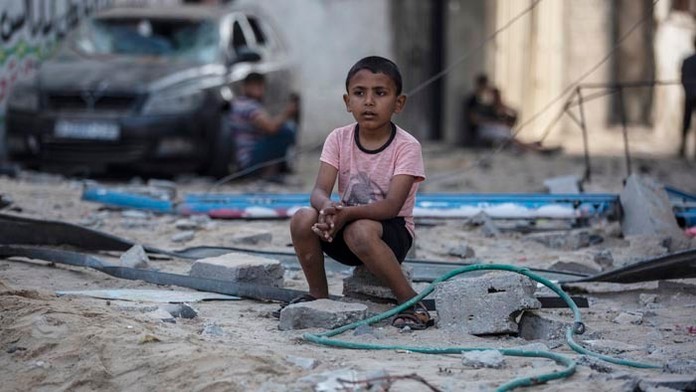 Palestínsky chlapec sedí na troskách zo zničených domov.