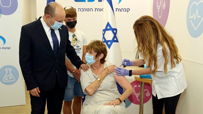 Izraelský premiér Naftali Bennett (vľavo) robí sprievod svojej matke Mirne Bennettovej, ktorá dostáva tretiu dávku vakcíny.