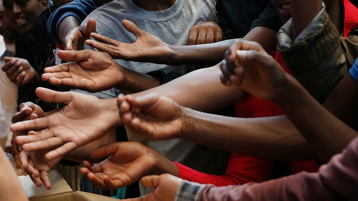 Migranti naťahujú ruky na centrálnej milánskej železničnej stanici, aby dostali jedlo. 11. jún