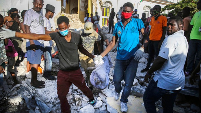Ľudia vynášajú telo, ktoré našli v ruinách domu po zemetrasení v meste Les Cayes.