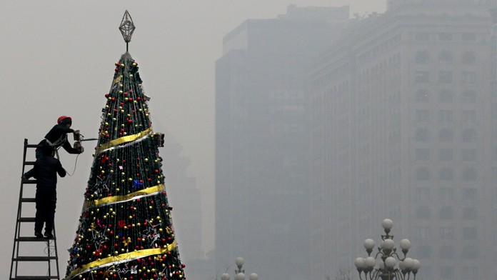 Zamestnanec zdobí vianočný stromček pred nákupným centrom počas smogovej pohotovosti v Pekingu.