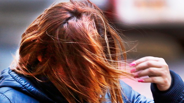 Mladá žena sa pokúša upraviť si účes v prudkom vetre. 