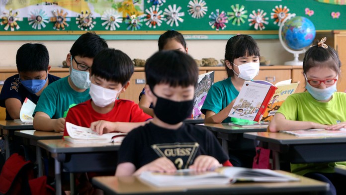 Žiaci základnej školy s ochrannými rúškami na tvári ako prevenciou pred blízkovýchodným resperačným syndrómom sedia počas vyučov