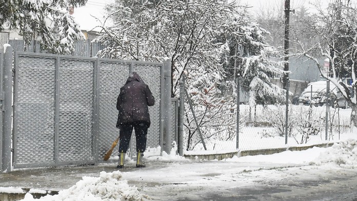 Žena odpratáva sneh z chodníka pred domom.