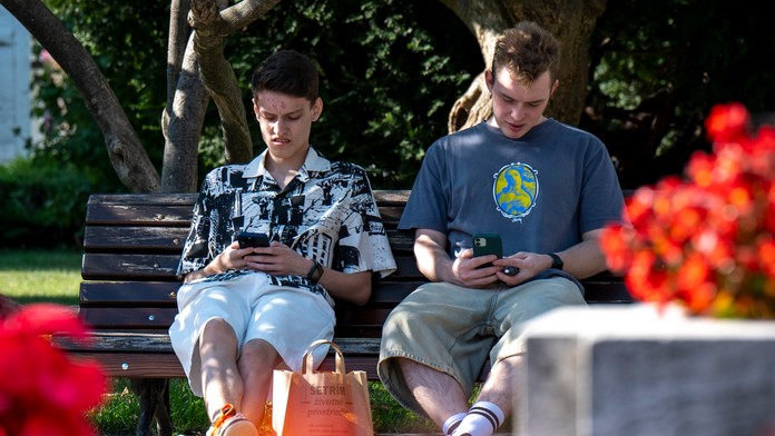 Na snímke mladí muži trávia čas na smartfónoch v Južnom parku počas horúčav v Prešove 13. augusta 2024.