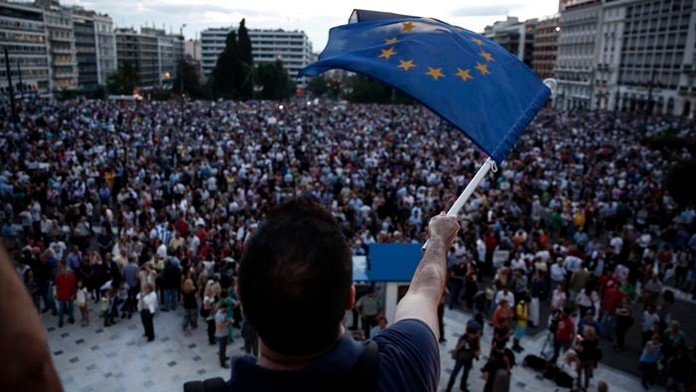 Demonštrant máva gréckou vlajkou počas zhromaždenia pred parlamentom v Aténach.