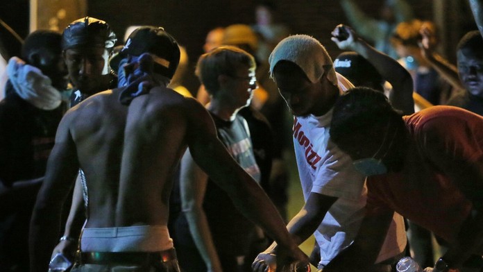 Maskovaní rasovo motivovaní demonštranti si pripravujú zápalné fľaše proti policajtom v americkom meste Ferguson.