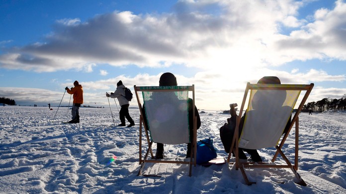 Ľudia sedia na slnku, ostatní sa lyžujú počas slnečného počasia v Helsinkách.