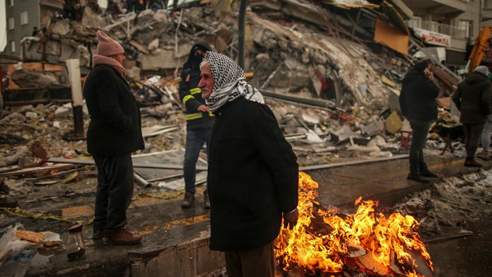 Ľudia sa zohrievajú pri zrútenej budove v tureckej Malatyi.